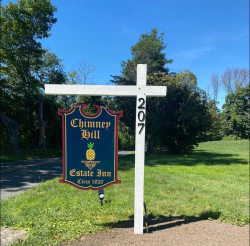 Sign for Chimney Hill Estate Inn, featuring a pineapple design, located at 207, with a green landscape in the background.