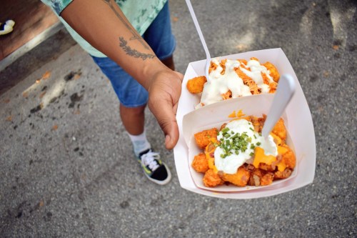 A person holds two containers of loaded tater tots topped with cheese, sour cream, and green onions.