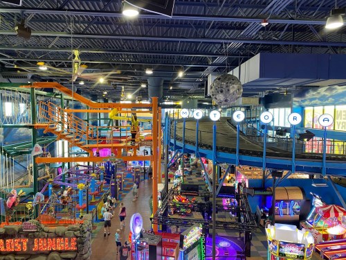 A vibrant indoor amusement park with colorful rides, arcade games, and a large hanging moon decoration.