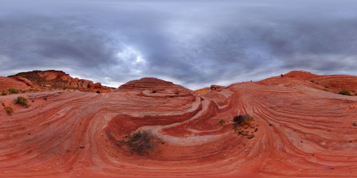 A panoramic view of red rock formations with swirling patterns under a cloudy sky.