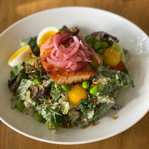 A vibrant salad topped with grilled salmon, pickled onions, soft-boiled eggs, and mixed greens in a white bowl.