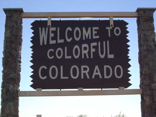 Sign reading "Welcome to Colorful Colorado" against a clear blue sky.