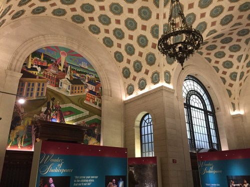 Interior of a grand hall featuring ornate ceiling, large windows, and colorful murals, with exhibition displays in the foreground.