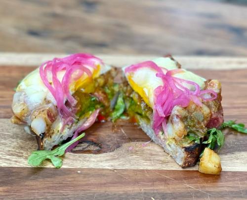 A cross-section of a sandwich filled with colorful ingredients, topped with pickled onions, on a wooden cutting board.