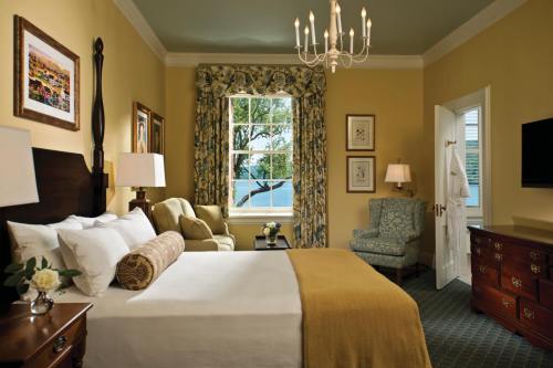 Cozy hotel room with a bed, armchairs, a chandelier, and a window with floral curtains, featuring warm yellow walls.