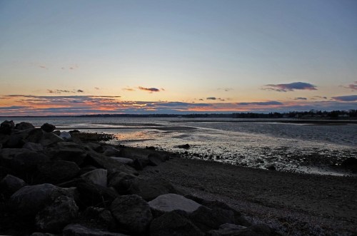 Sunset over a calm river, with rocky shorelines and scattered clouds in the sky.