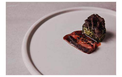 A gourmet dish featuring sliced beef, a layered vegetable stack, and a garnish of truffles on a minimalist plate.