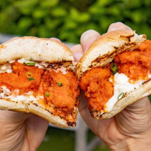 A close-up of a split sandwich filled with crispy orange chicken and creamy sauce, held by two hands.
