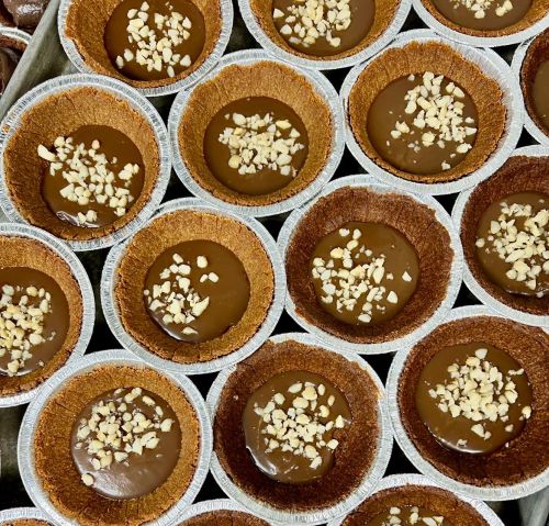 A close-up of mini chocolate tarts with a nut topping in silver foil cups, arranged in a circular pattern.