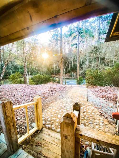 A serene view from a wooden porch, featuring a stone path leading to a river, surrounded by trees and autumn leaves.