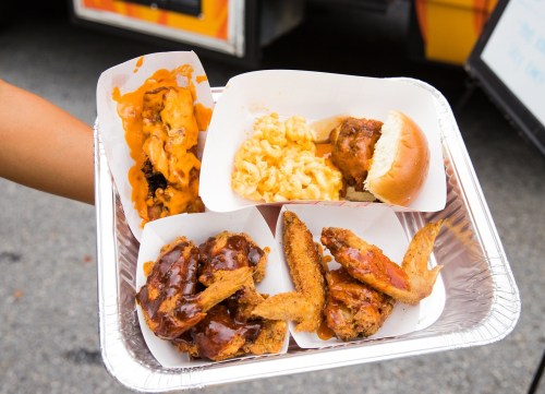 A tray of assorted comfort food featuring chicken wings, macaroni and cheese, a sandwich, and fried items.