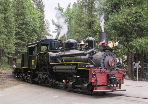 A vintage steam locomotive with smoke rising, surrounded by tall green trees.