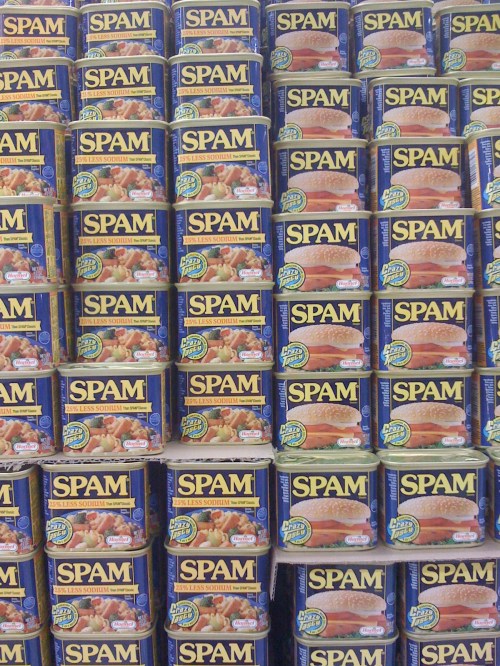 A stacked display of blue cans of Spam, showcasing multiple rows in a grocery store setting.