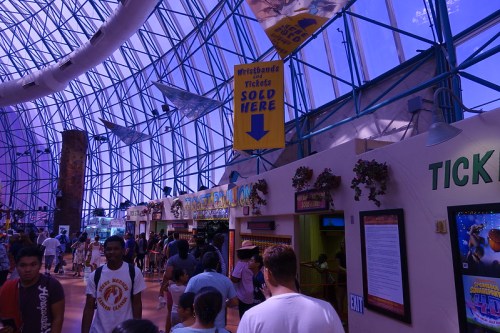 Interior of a ticketing area in a large, colorful venue with people and a sign indicating ticket sales.