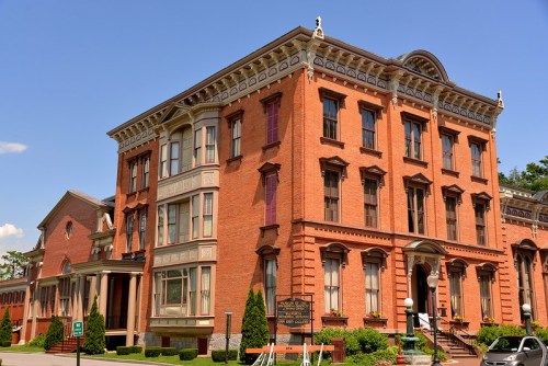 Historic red brick building with ornate architectural details, surrounded by greenery and a clear blue sky.