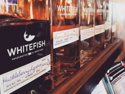 Bottles of Whitefish spirits lined up on a shelf, showcasing various flavors and handcrafted labels.
