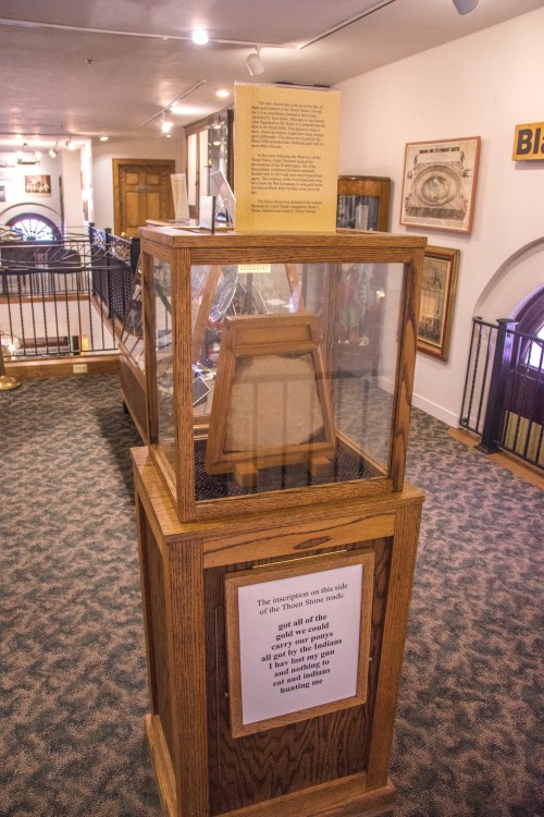 Display case in a museum showcasing an exhibit, with informational signs and a wooden stand inside.