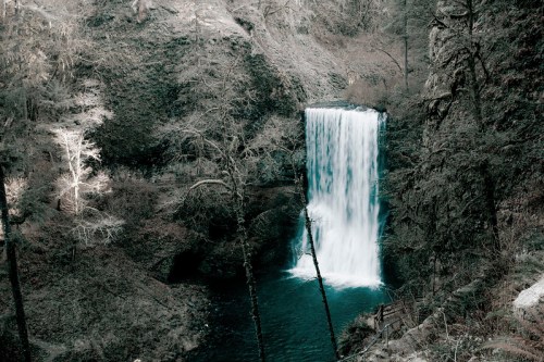 A serene waterfall cascades into a tranquil pool, surrounded by rocky cliffs and sparse trees.