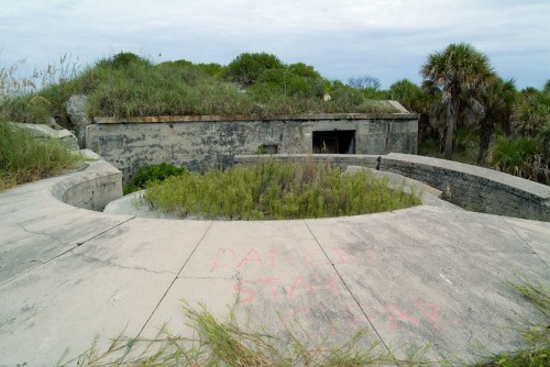 Abandoned concrete structure overgrown with grass, featuring a warning painted on the ground: "DANGER STAY AWAY."