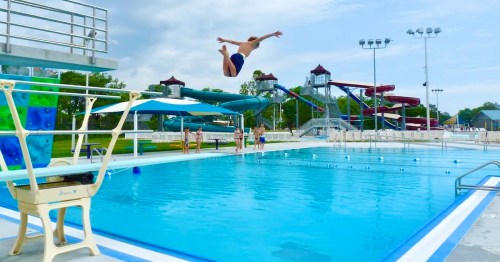A person dives into a swimming pool with water slides in the background on a sunny day.