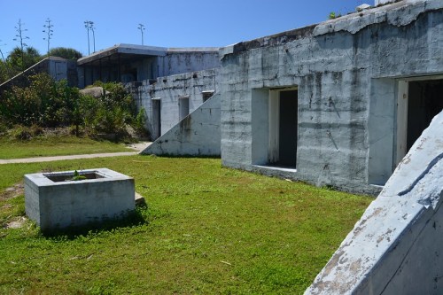 Abandoned concrete structures surrounded by grass and vegetation under a clear blue sky.