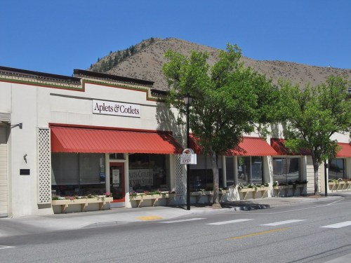 A storefront with a red awning, labeled "Aplets & Cotlets," surrounded by trees and mountains in the background.
