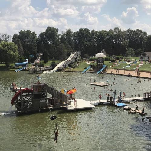 A busy water park with slides, a lake, and people swimming and enjoying the sun on a clear day.