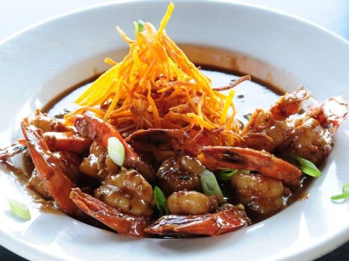 A plate of shrimp in a savory sauce, topped with crispy fried onions and garnished with green onions.