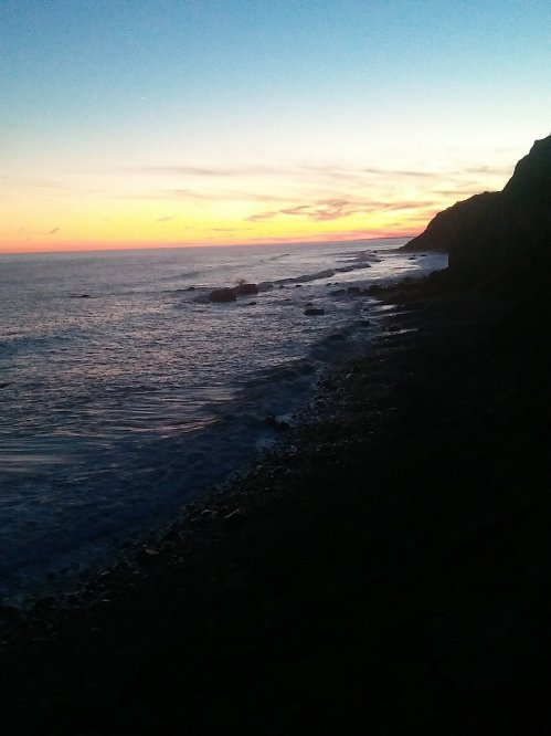 A serene coastal scene at sunset, with waves gently lapping against rocky shores and a colorful sky.