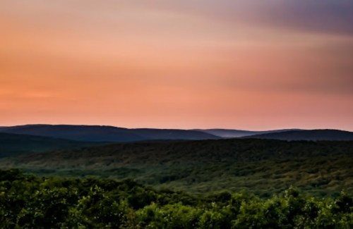 A serene landscape of rolling hills under a colorful sunset sky, with lush greenery in the foreground.