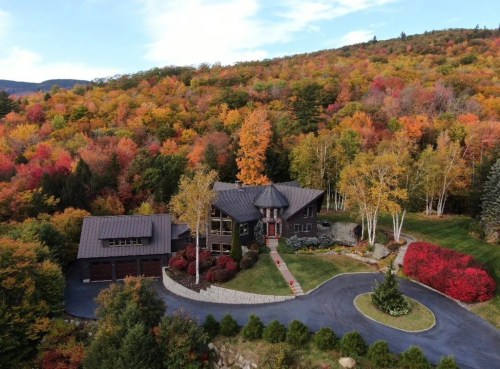 Aerial view of a modern house surrounded by vibrant autumn foliage and a winding driveway.