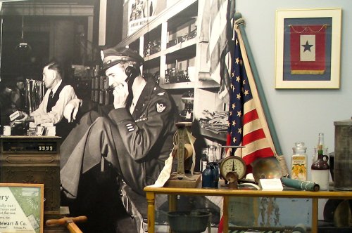 A historical display featuring a black-and-white photo of a soldier, vintage items, and an American flag.
