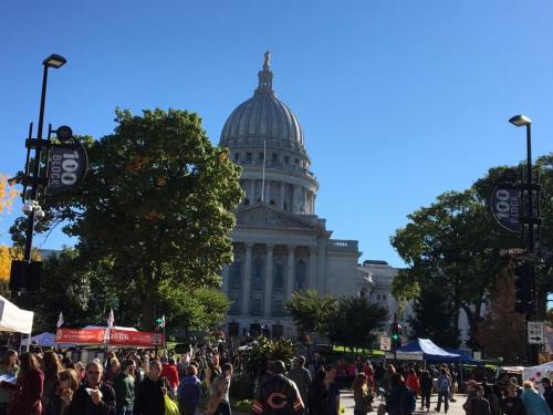 Crowd gathered in front of a large, domed building on a sunny day, with trees and tents visible in the foreground.
