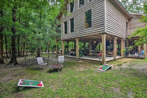 A wooden house surrounded by trees, featuring a fire pit and cornhole boards on the grassy yard.