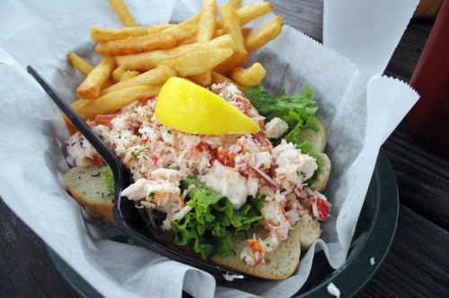 A lobster roll with lettuce and a lemon wedge, served with a side of golden French fries.