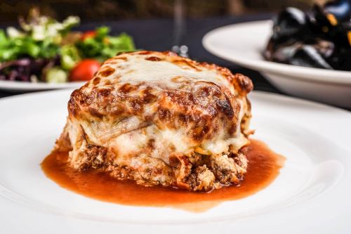 A serving of lasagna topped with melted cheese, served with a side of salad and mussels on a white plate.