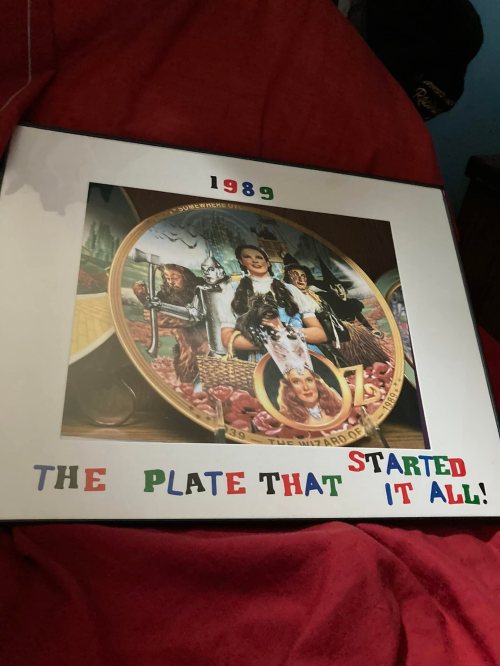 A framed decorative plate with colorful text reading "1989 THE PLATE THAT STARTED IT ALL!" on a red background.