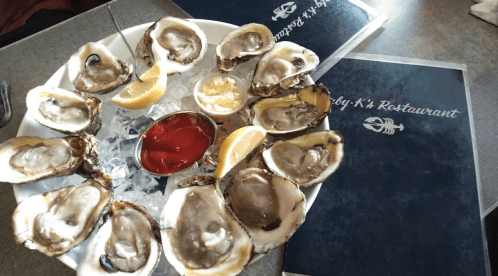 A plate of fresh oysters on ice, garnished with lemon wedges and cocktail sauce, alongside restaurant menus.