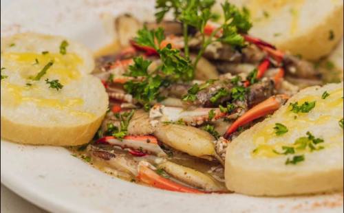 A plate of sautéed seafood with herbs and spices, served with slices of garlic bread.