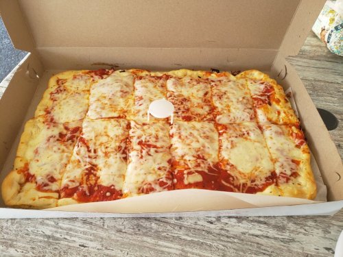A large pizza in a box, topped with melted cheese and tomato sauce, cut into rectangular slices.
