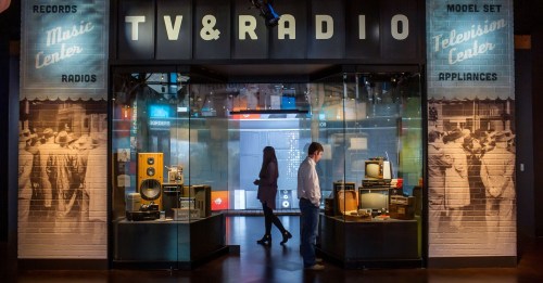 A museum exhibit showcasing vintage radios and televisions, with visitors exploring the displays.