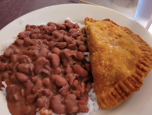 A plate with rice, red beans, and a golden-brown empanada on the side.
