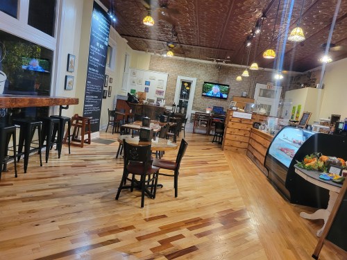 Cozy restaurant interior with wooden floors, tables, and a display case, featuring warm lighting and decorative elements.