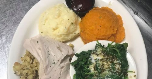 A plate with turkey, stuffing, mashed potatoes, sweet potatoes, and sautéed spinach with a side of barbecue sauce.