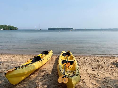 Two yellow kayaks on a sandy beach, with calm water and a distant island under a clear sky.
