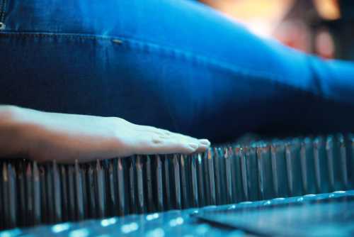 A hand resting on a bed of sharp pencils, with a person's leg visible in the background.