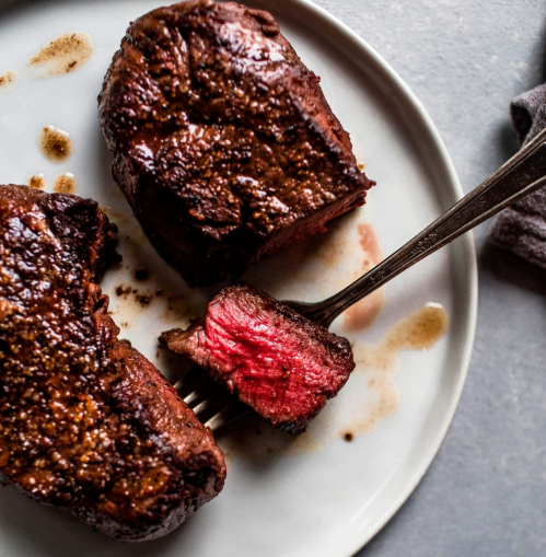 A plate with three pieces of perfectly cooked steak, one sliced to reveal a pink interior, with a fork beside it.