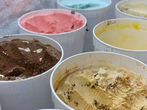 Various tubs of ice cream in different flavors, including chocolate, strawberry, and yellow, arranged in a row.