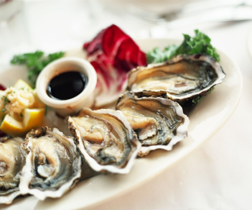 A plate of fresh oysters served with lemon, dipping sauce, and garnished with greens and lettuce.
