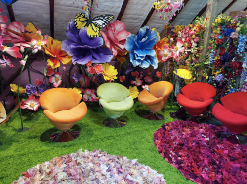 Colorful seating in a vibrant floral-themed room with large paper flowers and a green carpet.